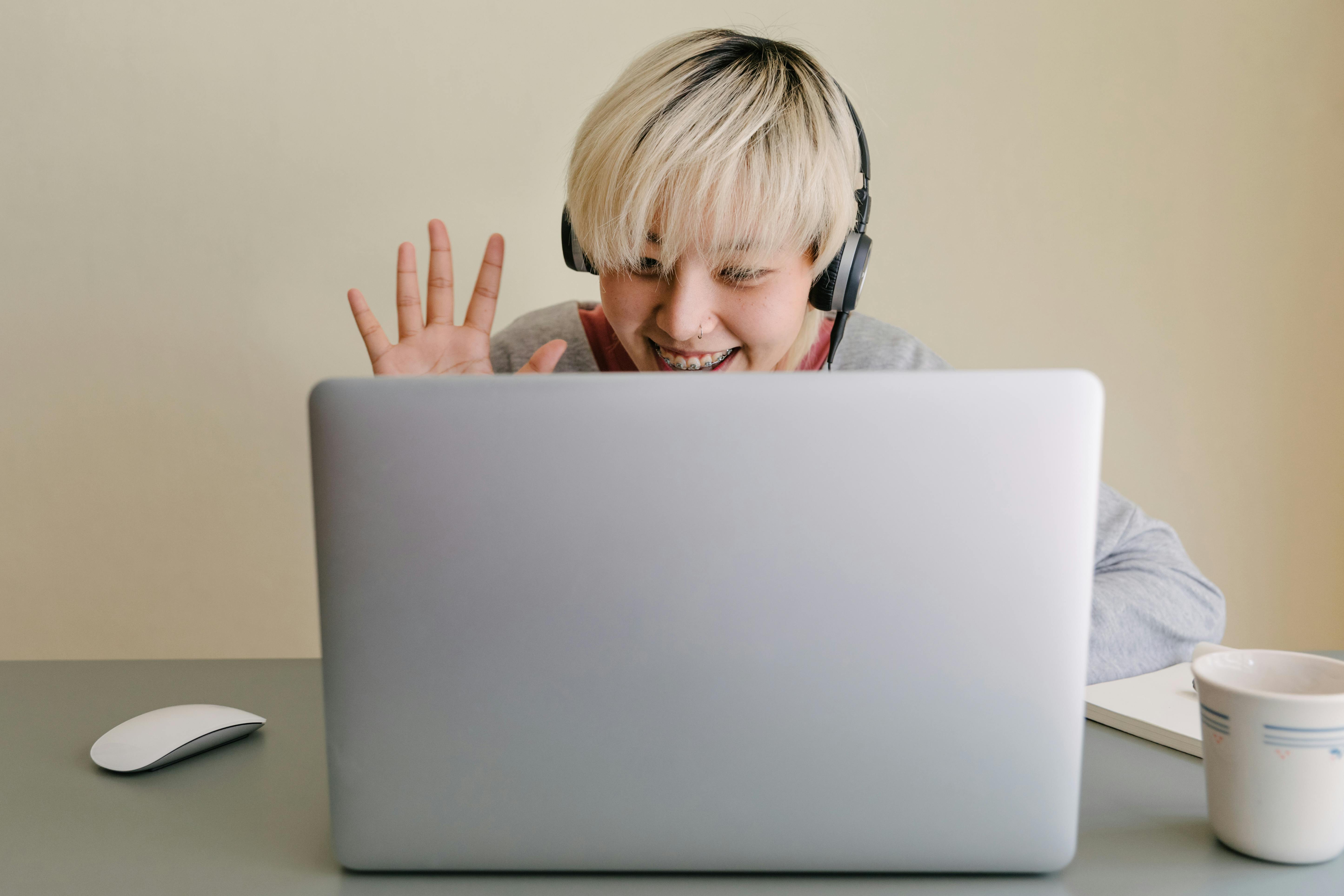 lady waving with her hand and smiling to the laptop camera (on a call with someone)