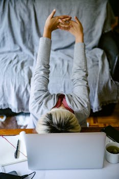 Overhead view of a woman stretching at her home workspace with a laptop.