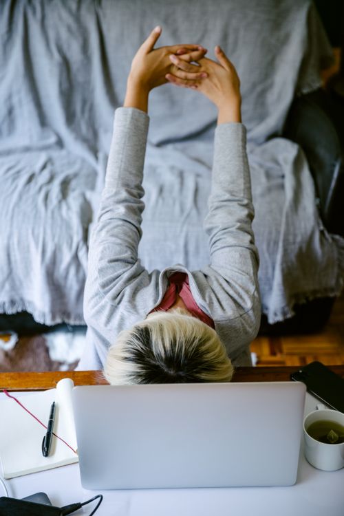 Free From above of exhausted unrecognizable female in casual clothes sitting at table with head on netbook keyboard and stretching arms behind back in living room Stock Photo