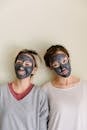 Young diverse women in casual clothes with black facial mud mask on beige background looking at camera