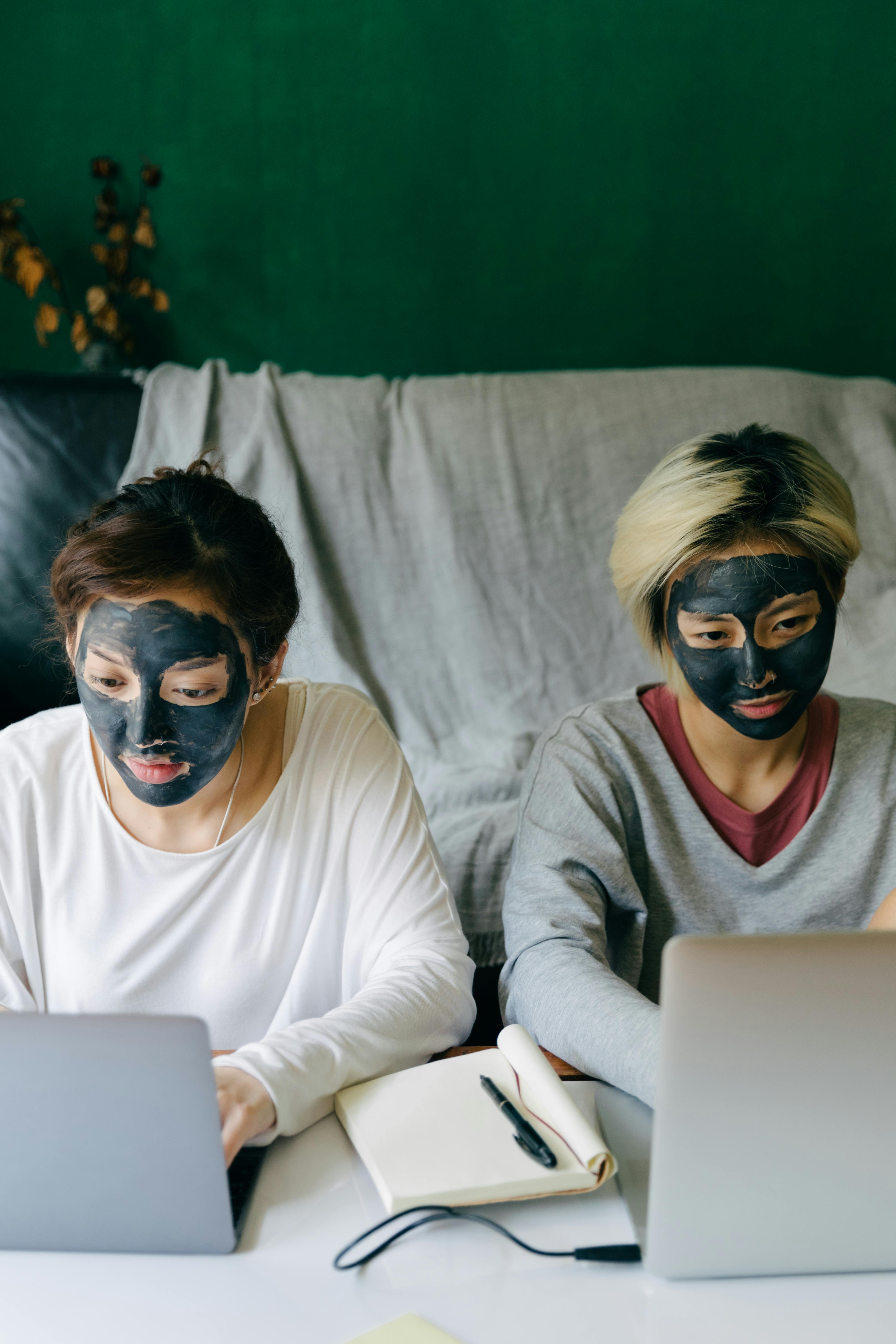 focused young women with black facial masks using laptops at home