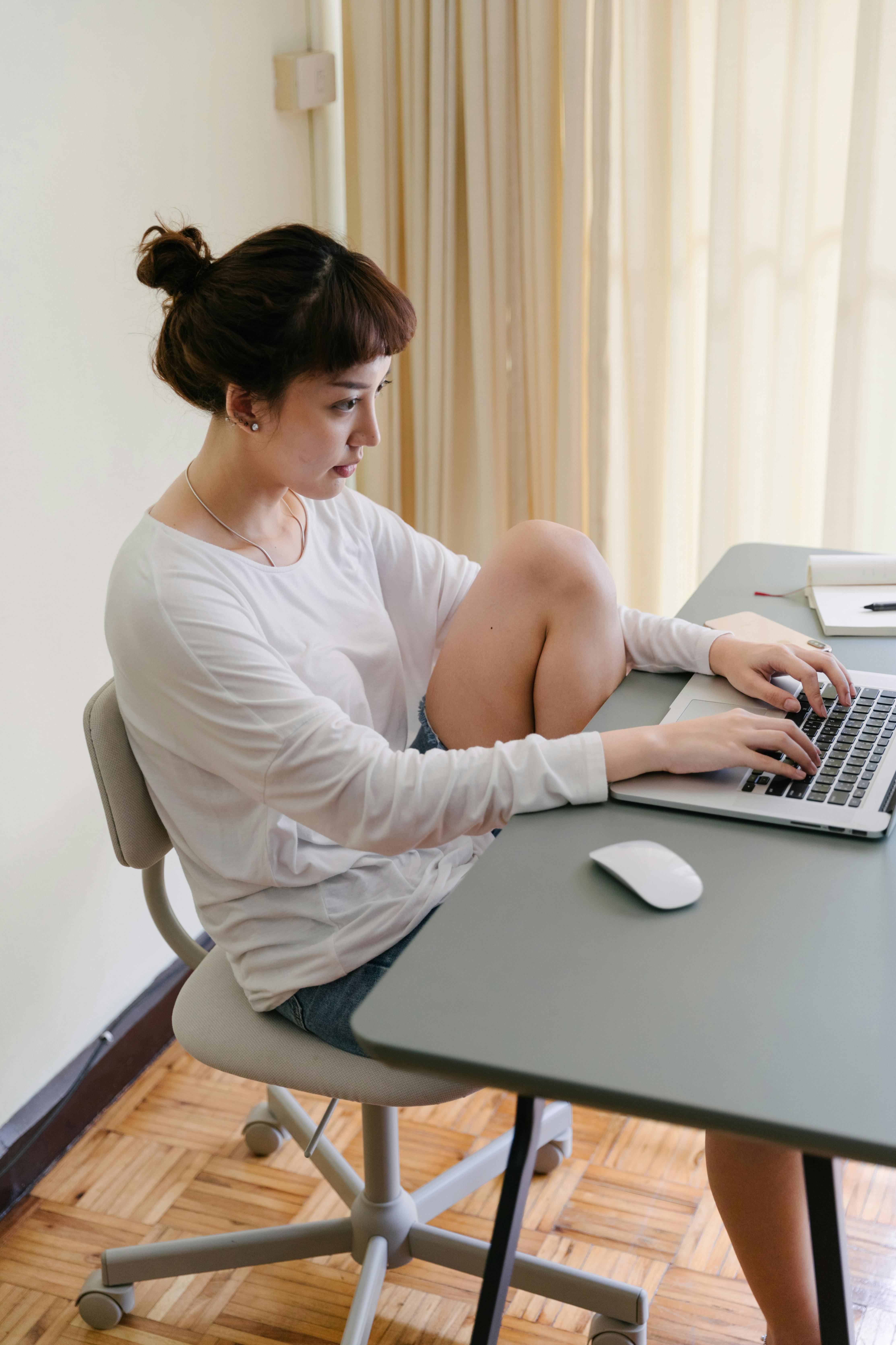 focused young asian woman sitting at table while using laptop at home