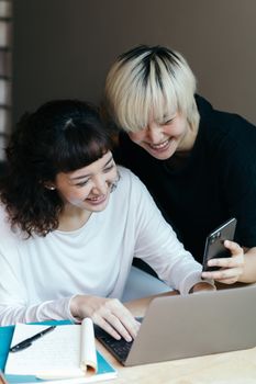 两名同事在室内兴奋地使用笔记本电脑和智能手机合作开展一个项目