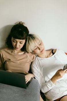 两名年轻女子在室内共用一副耳机，使用笔记本电脑和智能手机，一起放松身心