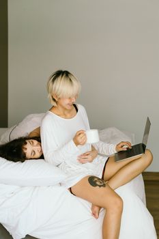 一对夫妇在床上舒适地分享着时光，一边用笔记本电脑，一边喝着咖啡