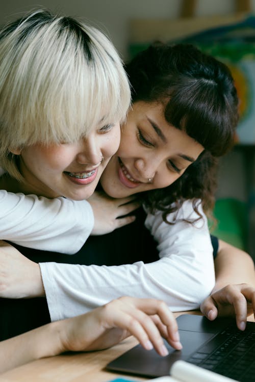 Happy friends cheerfully using laptop at table