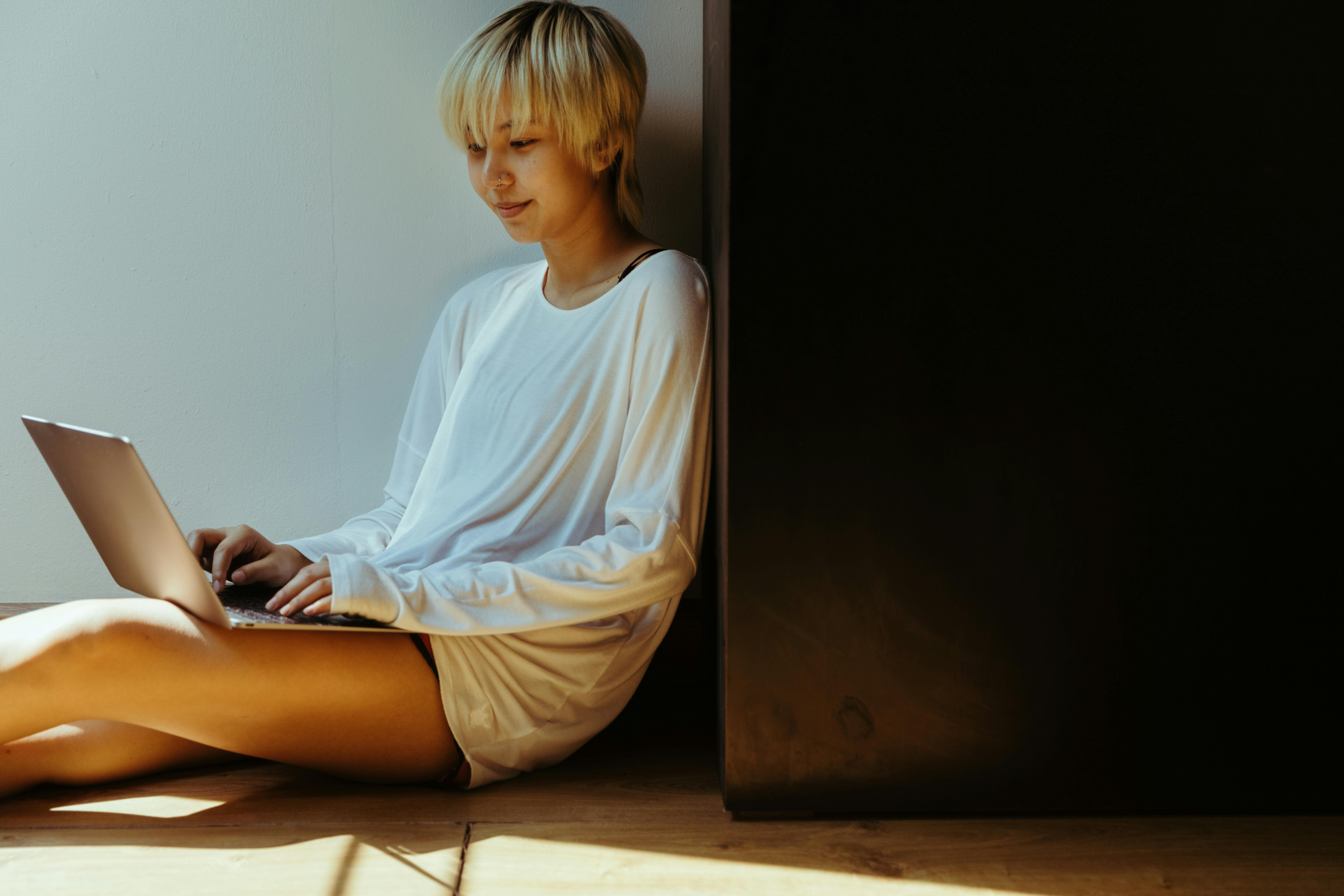 cheerful female freelancer typing on laptop while sitting on floor