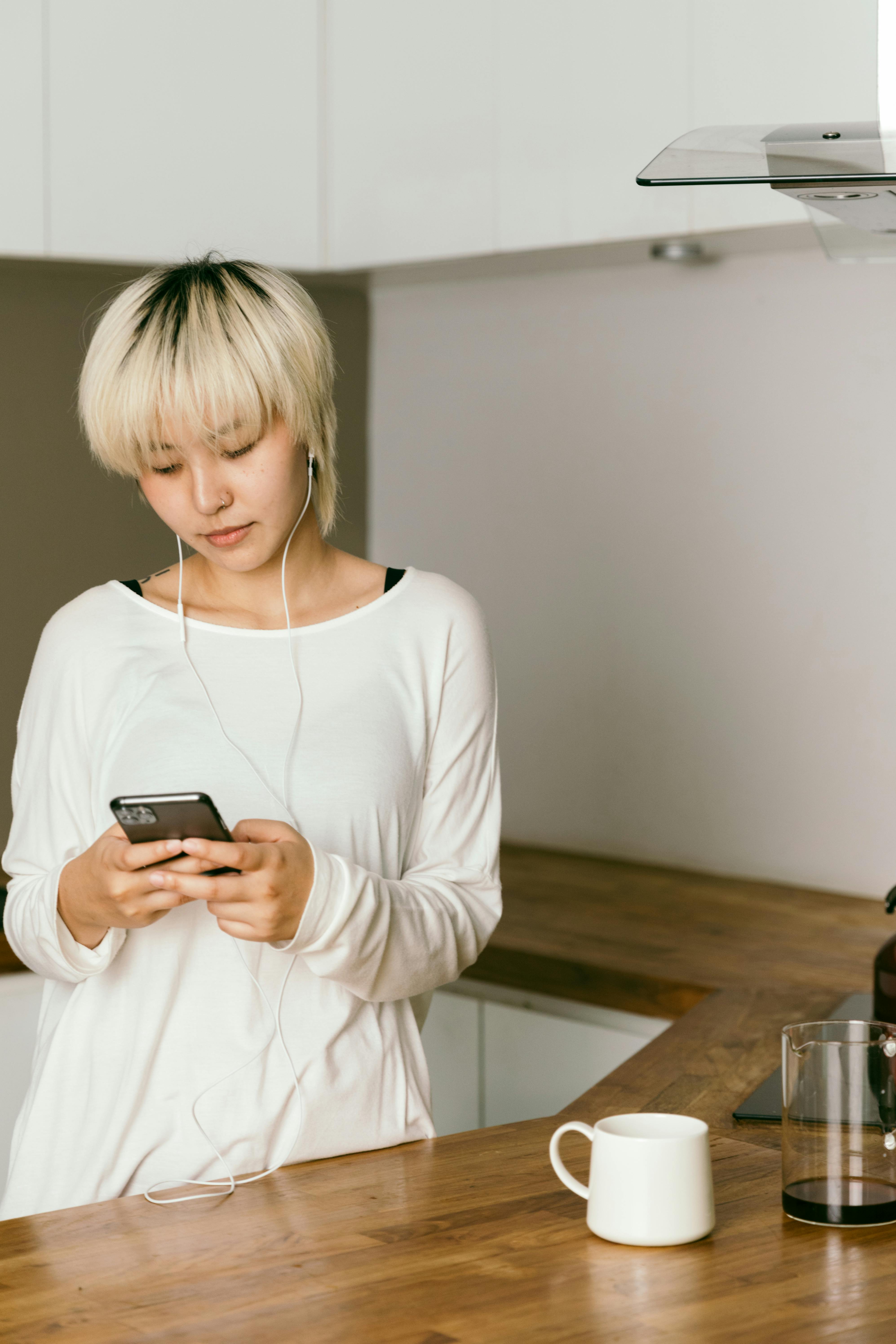 thoughtful woman in earbuds chatting on smartphone in kitchen