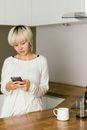 一位安静的年轻女子在现代化的厨房里用智能手机听音乐，象征着放松与科技的结合