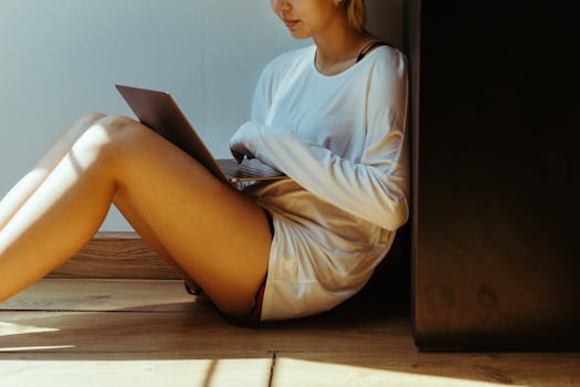 A woman sits on the floor, using a laptop in a serene home setting.