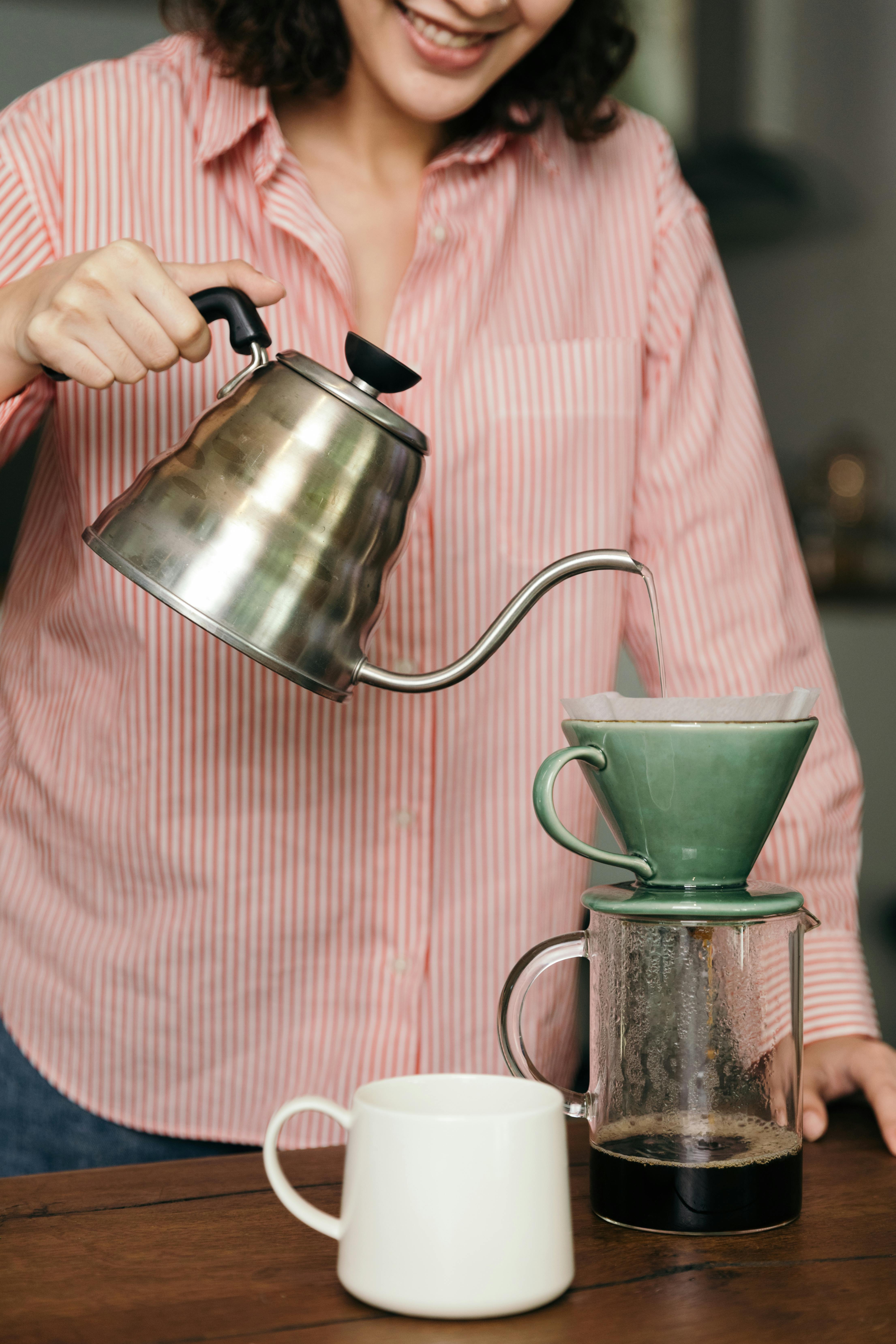 crop unrecognizable woman with kettle preparing fresh coffee in kitchen