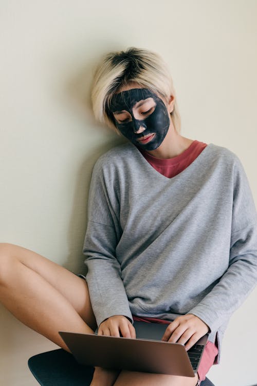 Female freelancer with clay mask on face typing on laptop