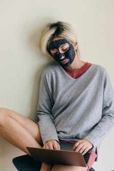 Young woman in casual wear with face mask working on laptop, enjoying serene home environment.