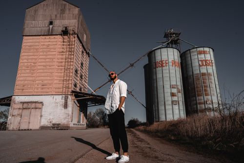 Free A fashionable man in sunglasses poses by industrial silos outdoors on a sunny day. Stock Photo