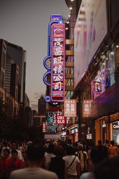 在上海热闹的夜色中，霓虹灯招牌和灯光明亮的建筑物下，人群正在购物