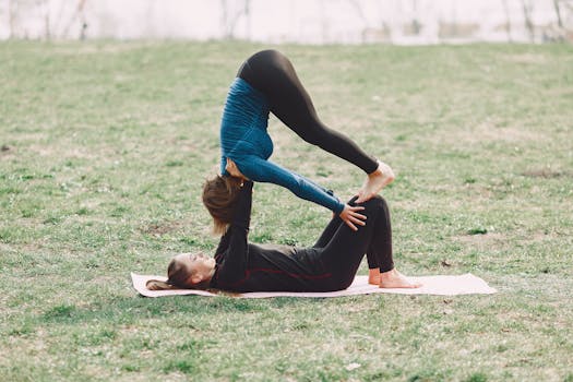 Young barefoot sportswomen in sportswear performing together acrobatic yoga exercise on mat during workout outdoors on green field adhering to healthy lifestyle