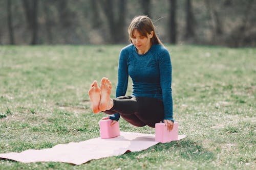 Full body barefoot sportswoman in sportswear doing yoga arm exercise on sport mat during training on lawn in park adhering to healthy lifestyle while looking down
