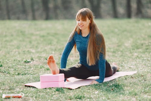 Positive young woman doing yoga with blocks on lawn