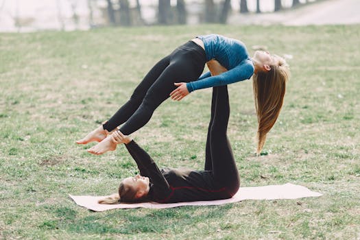 Two women performing acro yoga on a sunny day in the park, showcasing balance and flexibility.