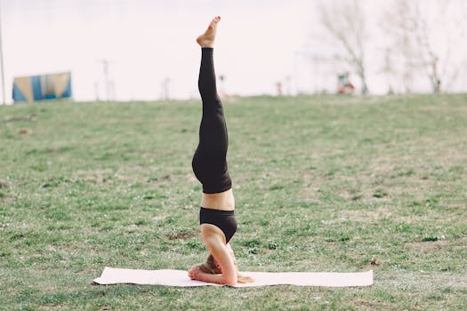 A woman performs a yoga headstand on a mat in a serene outdoor park.