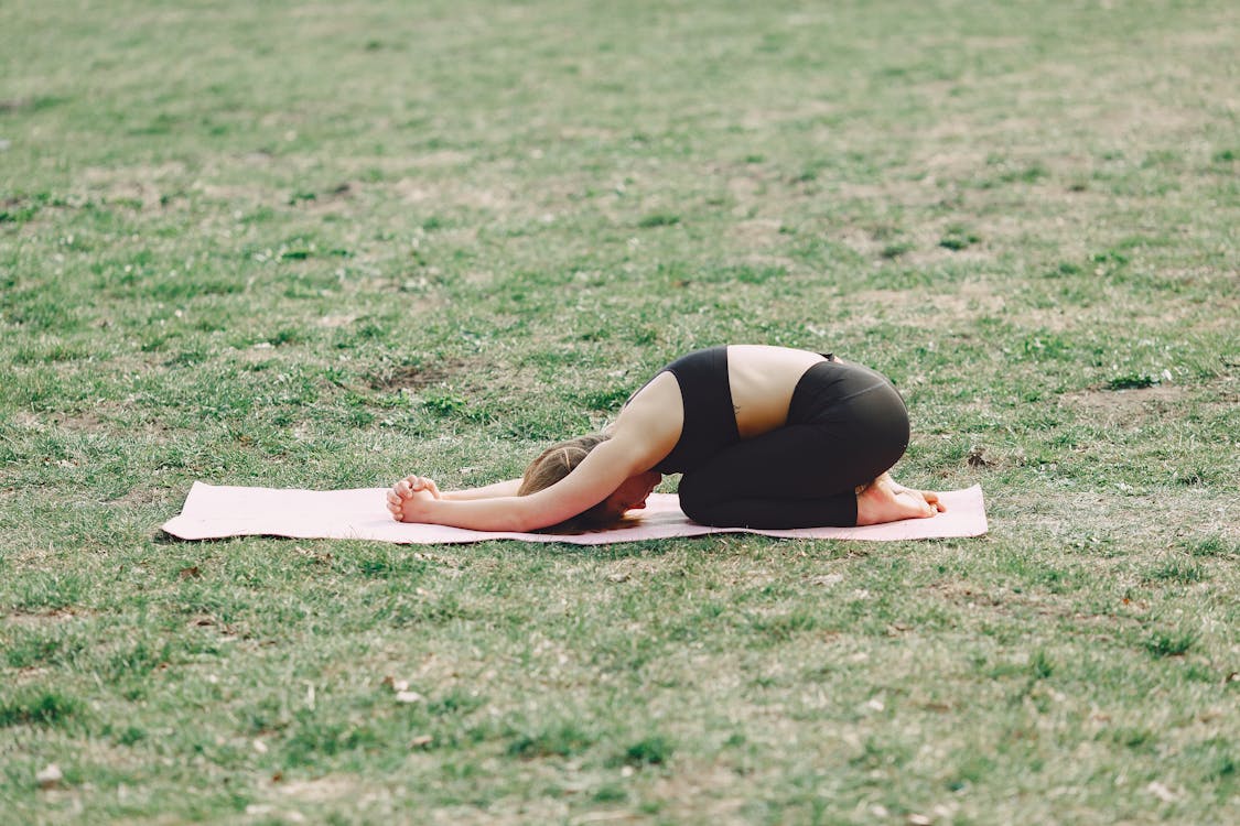 Relaxed barefoot woman performing yoga exercise on green field