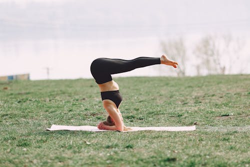 Free Side view of young sportswoman in black sportswear practicing headstand pose with L shape on sport mat during outdoors workout adhering to healthy lifestyle Stock Photo