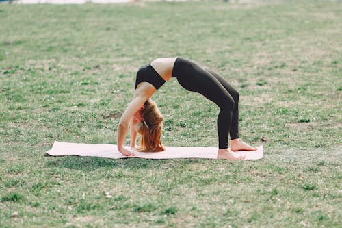 Free Side view of young sportswoman in black sportswear practicing wheel pose on sport mat during outdoors workout adhering to healthy lifestyle Stock Photo