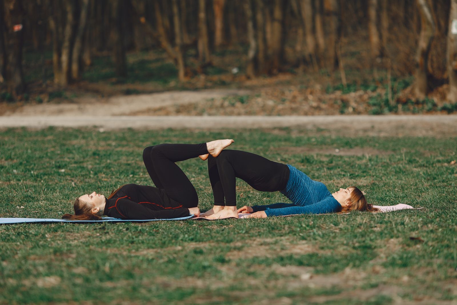 Two women practicing bridge pose together outdoors on yoga mats