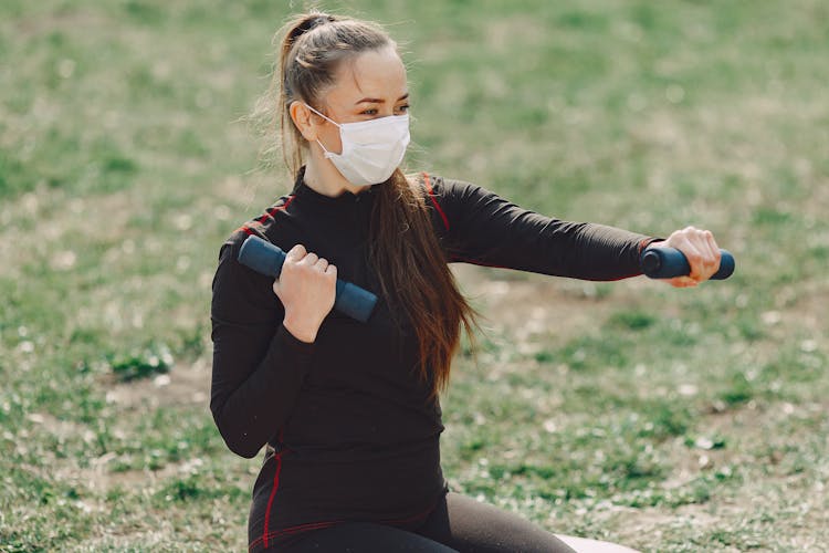 Sportswoman In Face Mask Exercising With Dumbbells Outdoors