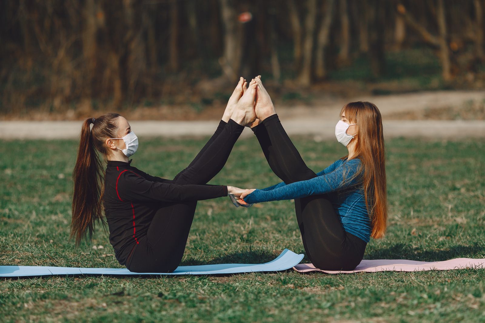 Two women practicing boat pose (Navasana) side by side to strengthen the core