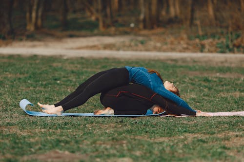 Woman stretching back and girlfriend lying in Childs pose outdoors