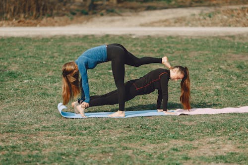 Free Side view of fit lady in sports clothes standing in Phalakasana pose and supporting slim unrecognizable girlfriend on mat in park in daylight Stock Photo