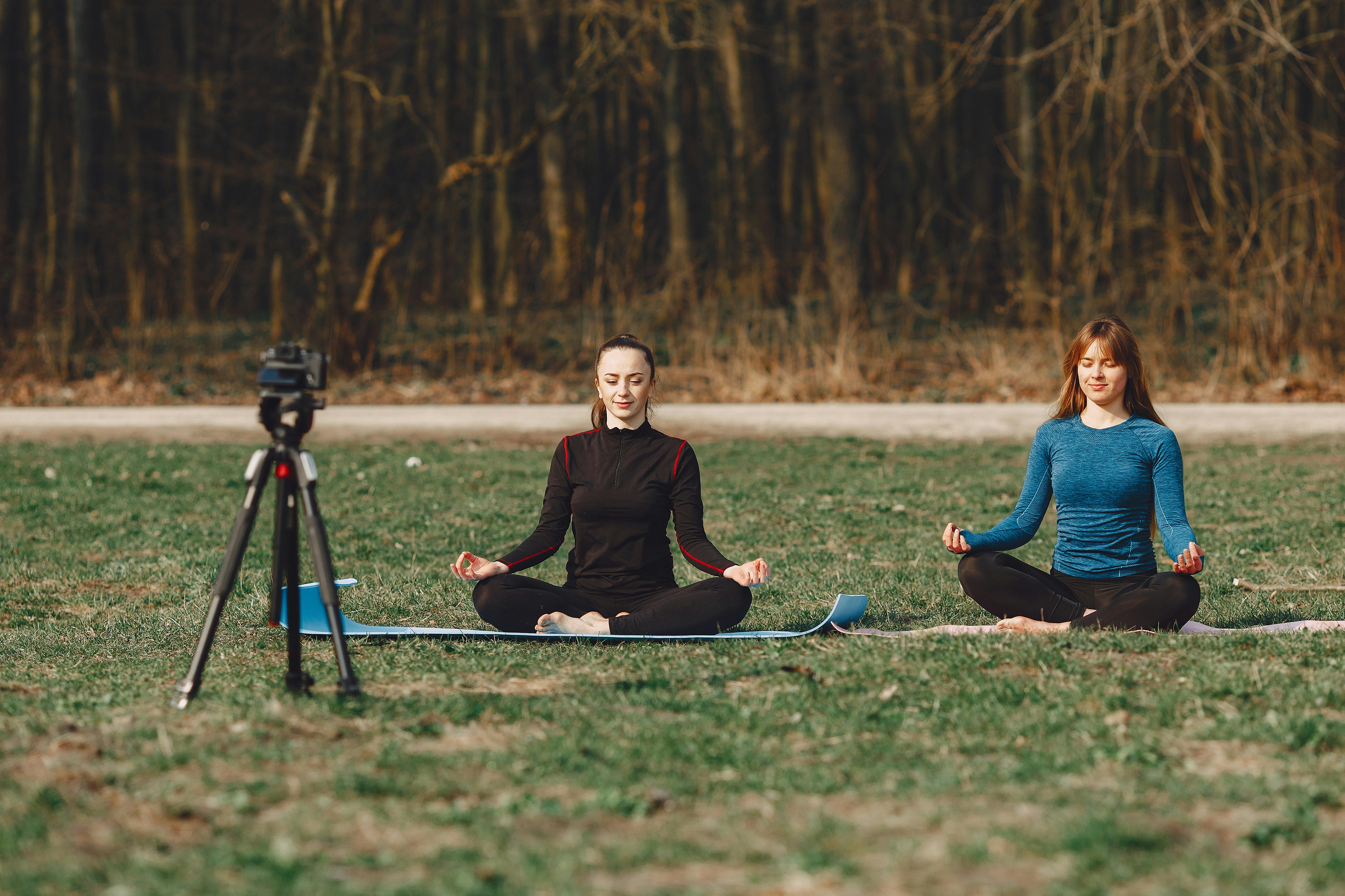 calm girlfriends sitting in lotus pose during meditation outdoors