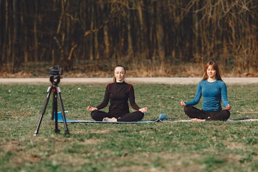 Two women practicing yoga meditation outdoors while recording with a camera.