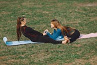 Happy girlfriends exercising on mat on grass in daylight