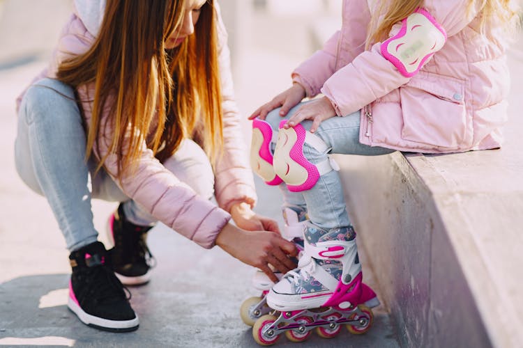 Crop Mother Preparing Daughter For Roller Skating