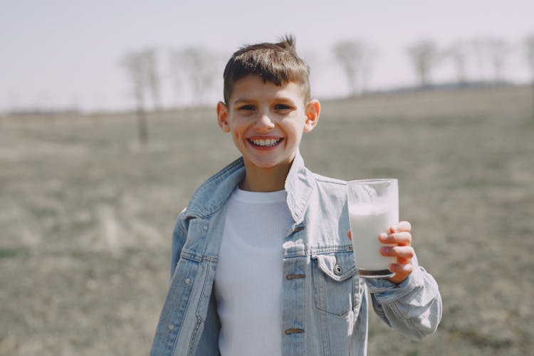 Happy Boy With Glass Of Milk In Countryside