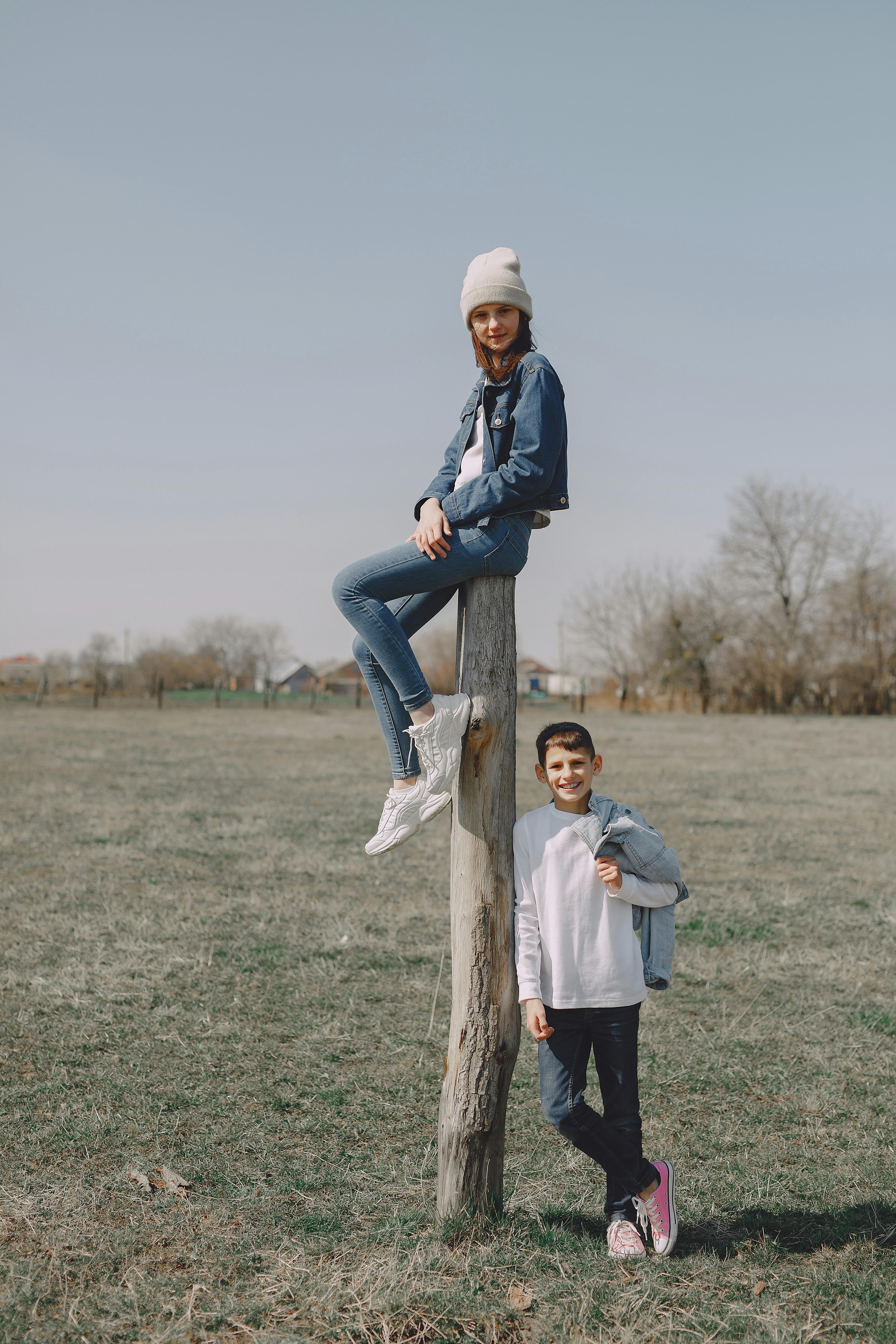 girl sitting on pillar and boy standing near in countryside