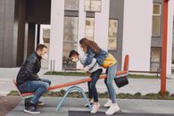 Family in mask swinging on seesaw on playground