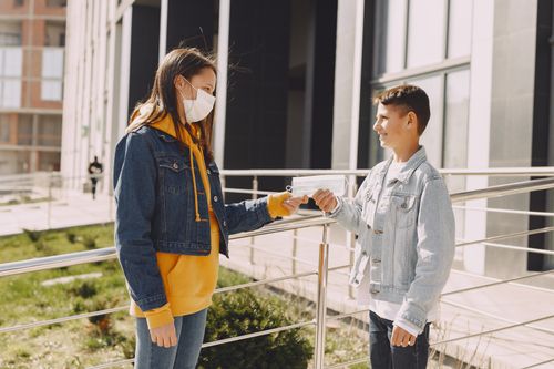 Free Side view of happy young boy in casual clothes smiling and standing against elder sister in medical mask on city street while taking face mask Stock Photo
