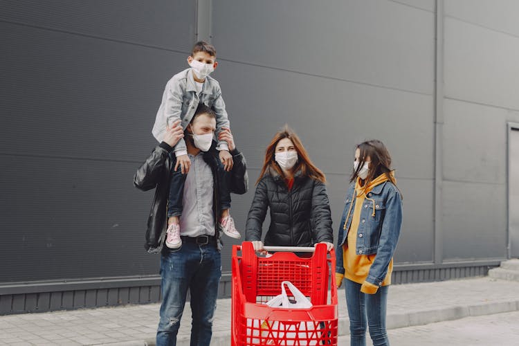 Family In Protective Masks With Trolley On Street