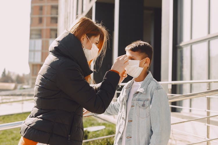 Woman Fixing Protective Mask On Kid Face