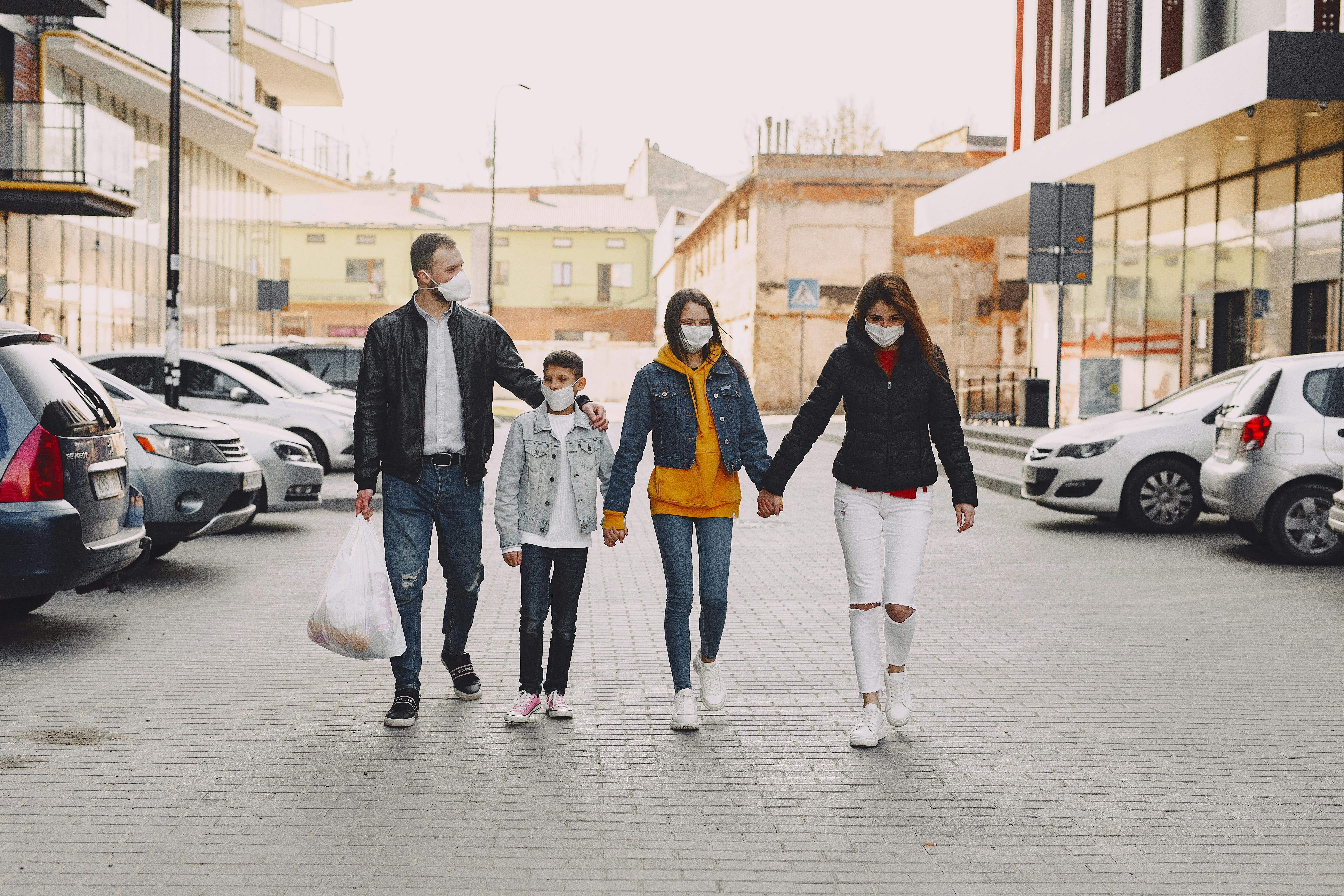 young family in medical masks walking along parking