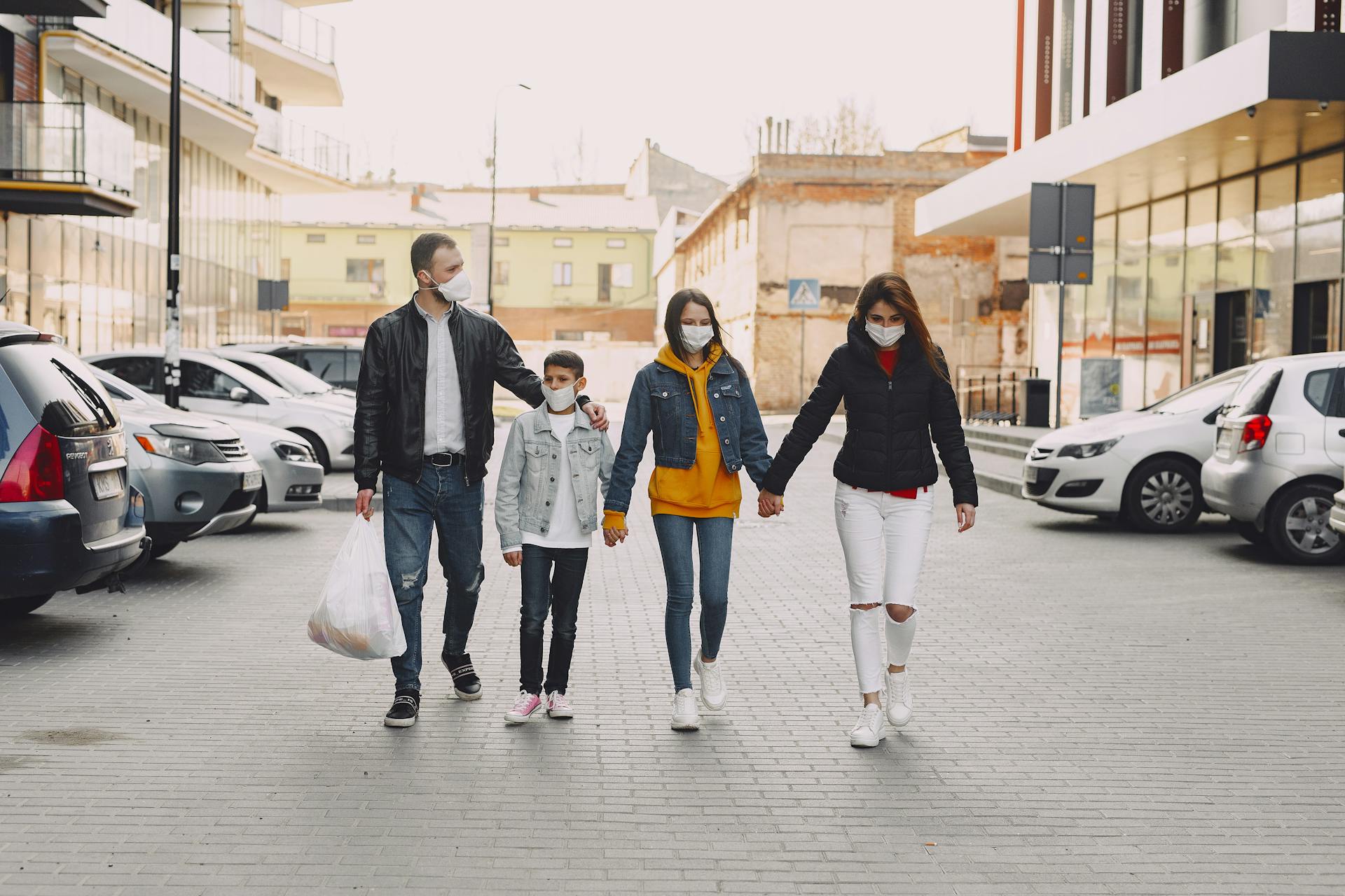 Young family in medical masks walking along parking