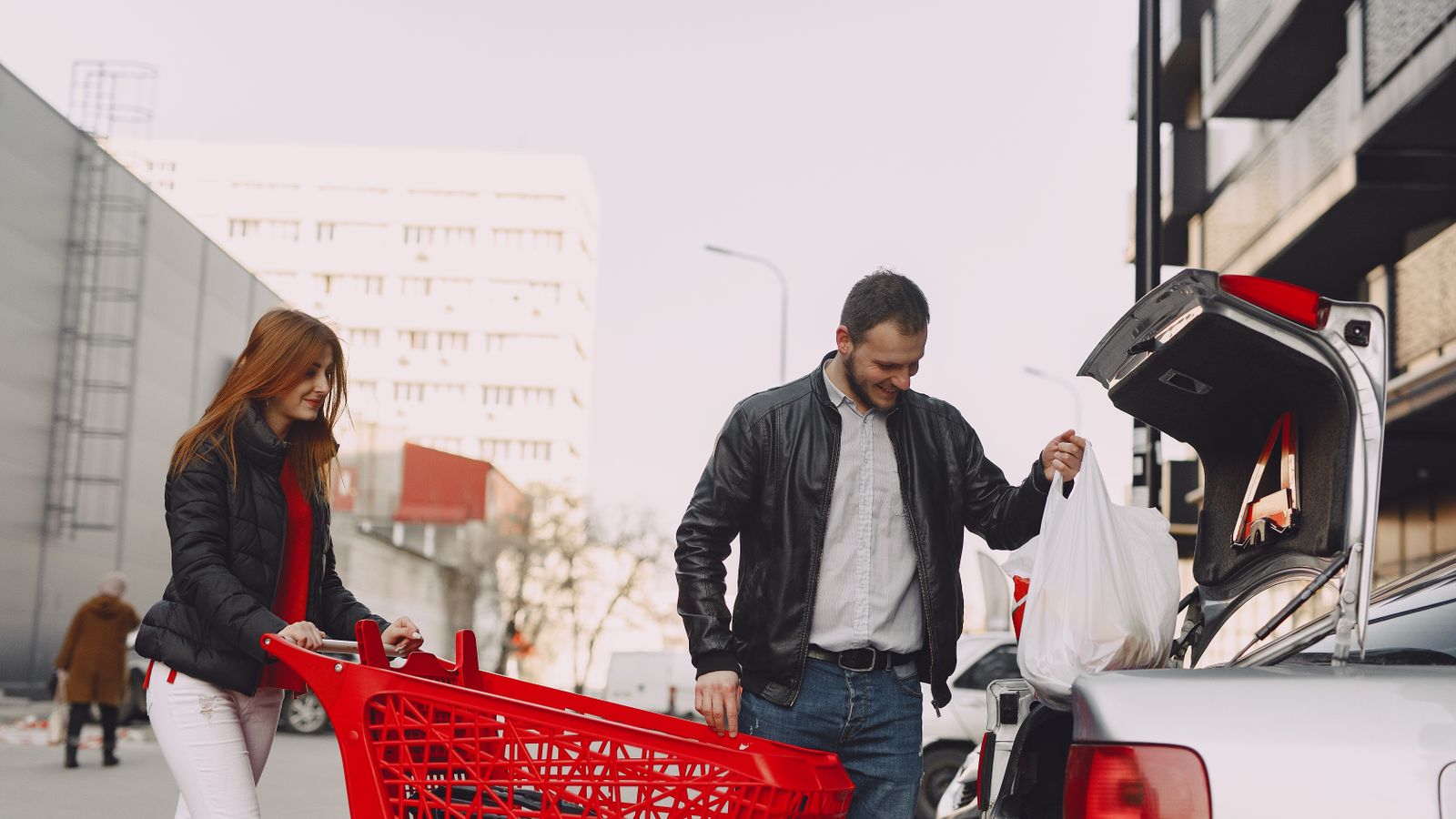 Two adults beside a shopping trolley loading a bag into a car