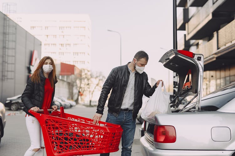 Couple In Protective Masks Moving Shopping Bags To Trunk