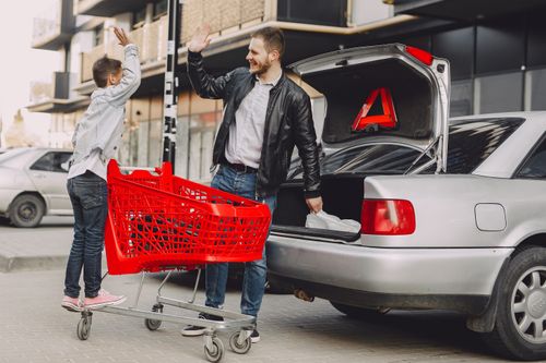 Free Full length of young father and little son in casual clothes giving high five to each other while moving shopping bags to trunk Stock Photo
