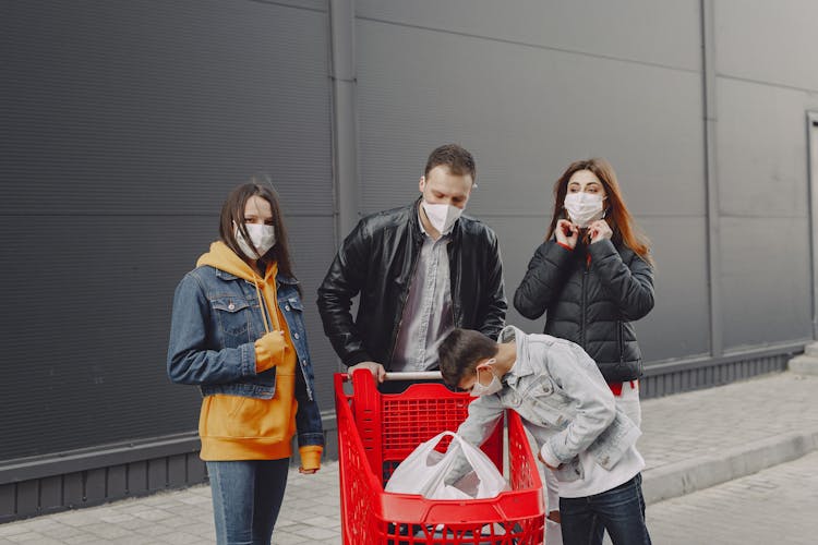 Young Family In Protective Masks With Shopping Trolley On Street