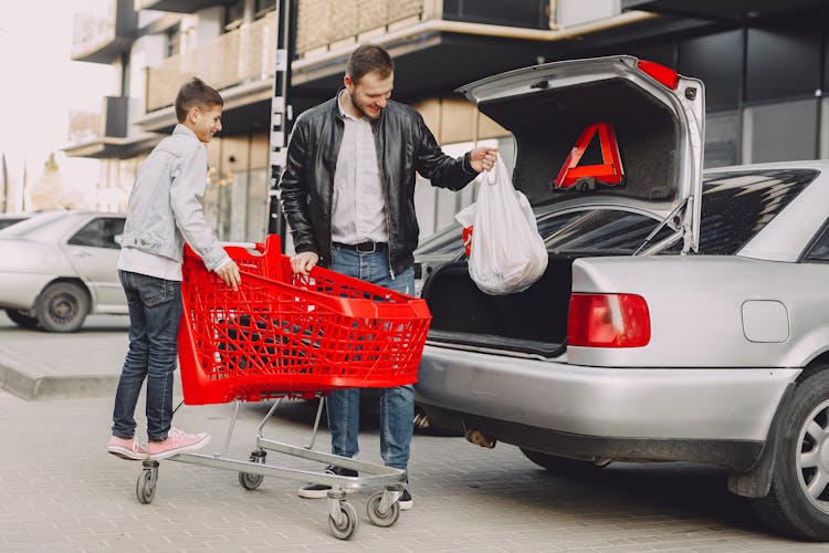 Man And Boy Putting Shopping Bag In Trunk