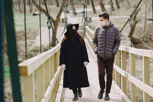A masked couple strolls on a wooden bridge in a park, observing social distancing guidelines.